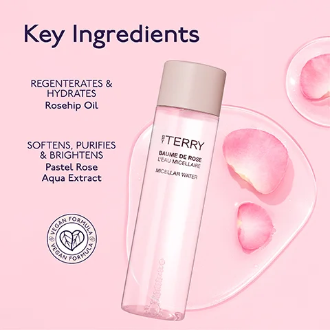 A By Terry Baume de Rose LEau Micellaire Micellar Water bottle stands on a clear surface with pink rose petals, alongside text that reads Key Ingredients, REGNERATES & HYDRATES Rosehip Oil, SOFTENS, PURIFIES & BRIGHTENS Pastel Rose Aqua Extract, and a circular badge with VEGAN FORMULA.