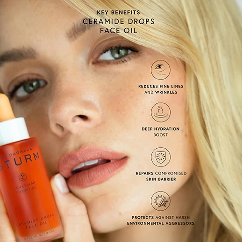 Image 2 - A blonde woman holds an orange Dr. Barbara Sturm Ceramide Drops Face Oil bottle near her face, with text overlaying the image that reads KEY BENEFITS CERAMIDE DROPS FACE OIL, DR. BARBARA STURM MOLECULAR COSMETICS CERAMIDE DROPS FACE OIL MADE IN GERMANY, REDUCES FINE LINES AND WRINKLES, DEEP HYDRATION BOOST, REPAIRS COMPROMISED SKIN BARRIER, PROTECTS AGAINST HARSH ENVIRONMENTAL AGGRESSORS. Image 3 - An orange dropper filled with a viscous liquid and bubbles is shown dripping onto a white, wavy surface, alongside text that reads: CERAMIDE DROPS FACE OIL, 98% AGREE¹, SKIN TEXTURE LOOKS AND FEELS SMOOTHER, SKIN FEELS PROTECTED AGAINST MOISTURE LOSS AND EXTERNAL AGGRESSORS², SKIN FEELS REPLENISHED AND PLUMPED, ¹ RESULTS FROM CONSUMER SELF-SCORING STUDY ON 51 PARTICIPANTS IN ONLY 28 DAYS, ² POLLUTION, HUMIDITY, LOW TEMPERATURES. Image 4 - A before and after comparison image shows the skin around an eye and nose; the left side, labeled Before, shows skin with visible pores and freckles, while the right side, labeled After 1 Application, shows the same area with skin appearing smoother and more radiant, accompanied by text that reads: CERAMIDE DROPS FACE OIL. Enhances hydration, radiance and smoothness for a healthier skin barrier - after just one application*. SCIENTIFICALLY PROVEN. IN JUST 1 APPLICATION, BOOSTS SKIN BARRIER, HYDRATION AND RADIANCE. *CLINICALLY-PROVEN RESULTS ON 31 PARTICIPANTS AFTER ONE APPLICATION AND AFTER 28 DAYS. Image 5 - A close-up of an orange bottle of Dr. Bare face oil with a dropper, alongside a list detailing its ingredients and their benefits, with text that reads: INGREDIENT SCIENCE CERAMIDE DROPS FACE OIL. SKIN IDENTICAL CERAMIDES: A 5-Ceramide Complex that helps strengthen and revitalize the natural skin barrier. PRECIOUS OILS: Argan, Evening Primrose and Sweet Almond Oils help restore the lipid barrier. ASTAXANTHIN: A potent antioxidant that protects the skin from premature skin aging. PHYTOSQUALANE: Reduces the appearance of fine lines and wrinkles. DR. BARE MOLECULAR COSMETICS. Image 6 - The image shows white cream swirls and orange-gold oil drops scattered around three white Dr. Barbara Sturm cosmetic jars, with text reading CERAMIDE DROPS FACE OIL, SUPER ANTI-AGING FACE CREAM, FACE CREAM, FACE CREAM RICH, and HOW TO USE: Add a few drops of the CERAMIDE DROPS FACE OIL to your favorite Dr. Barbara Sturm MOISTURIZER to boost skin barrier strength, improve hydration and promote elasticity.